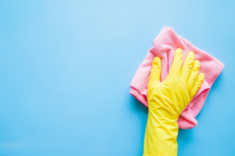 Does an AC Kill Mold? Hand in a yellow glove wiping a blue wall or table with a pink cloth.