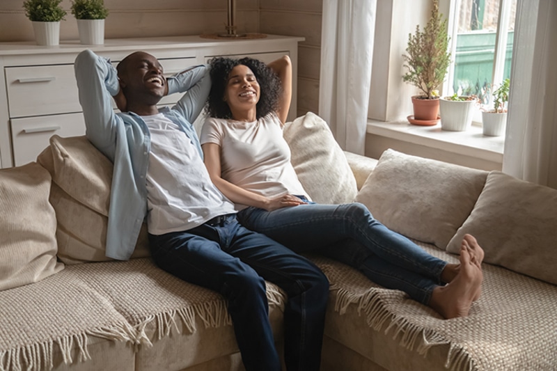 Happy young couple laid back on the couch, smiling.